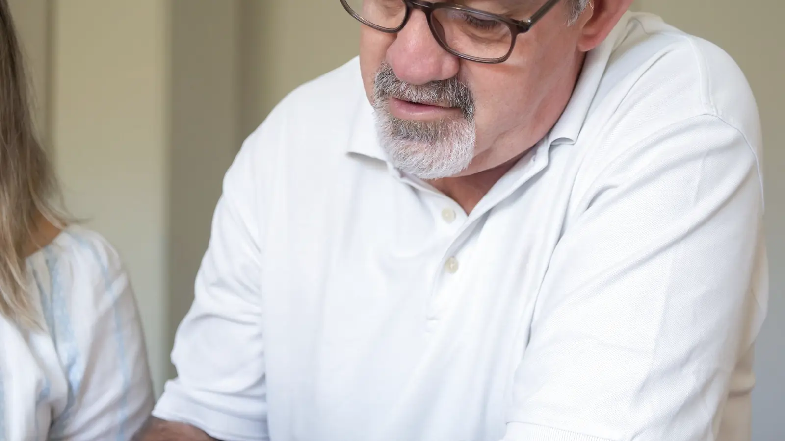 An older fair-skinned white man reviews a smartphone carefully at a wooden table