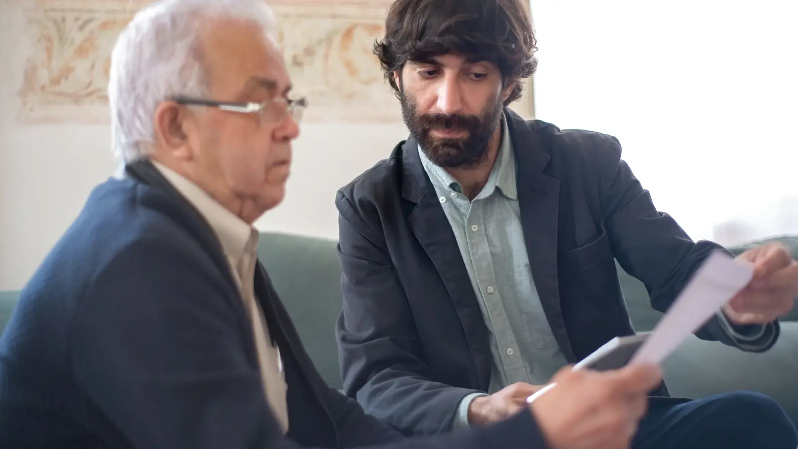 An older fair-skinned white adviser and a younger man review a document together during a careful consultation
